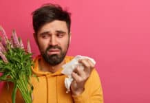 Allergy, sickness, bad feelings concept. Upset ill guy suffers from allergy on flower pollen, holds hygienic paper napkin, has runny nose and sneezing, has itchy eyes, being unhealthy, poses indoor