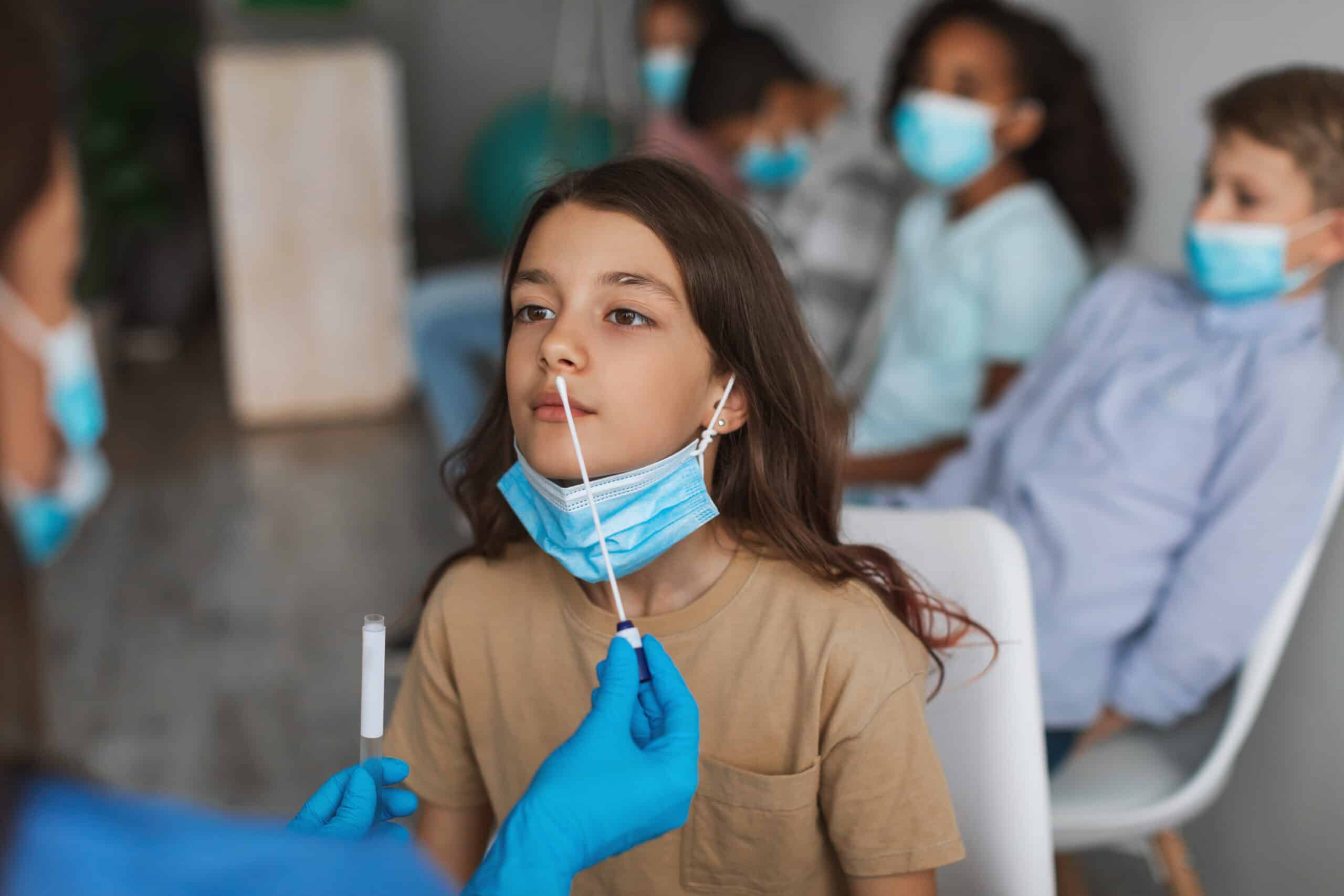 Girl Getting Tested For Coronavirus Sitting With Children Group Indoors