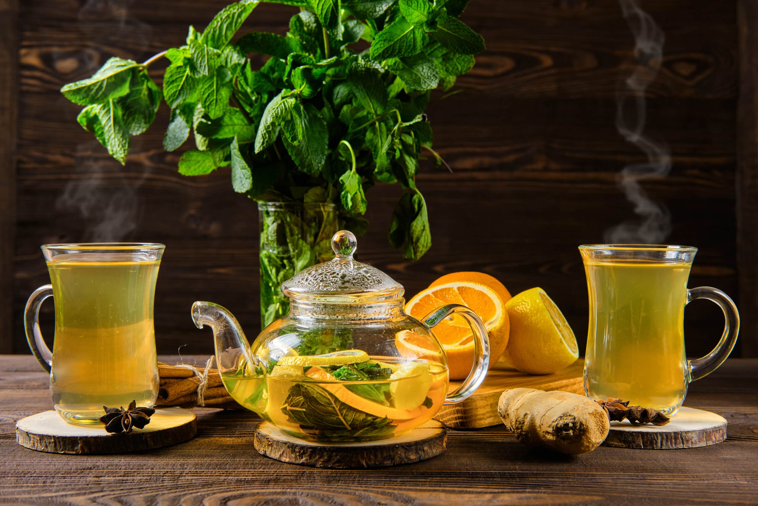 Hot tea with lemon, orange, ginger and mint on wooden table in the morning