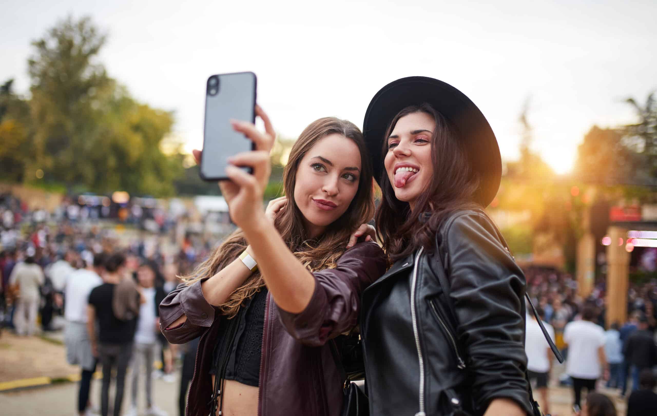 Joyful women taking selfies on smartphone fooling around and sticking out tongues in sunny day