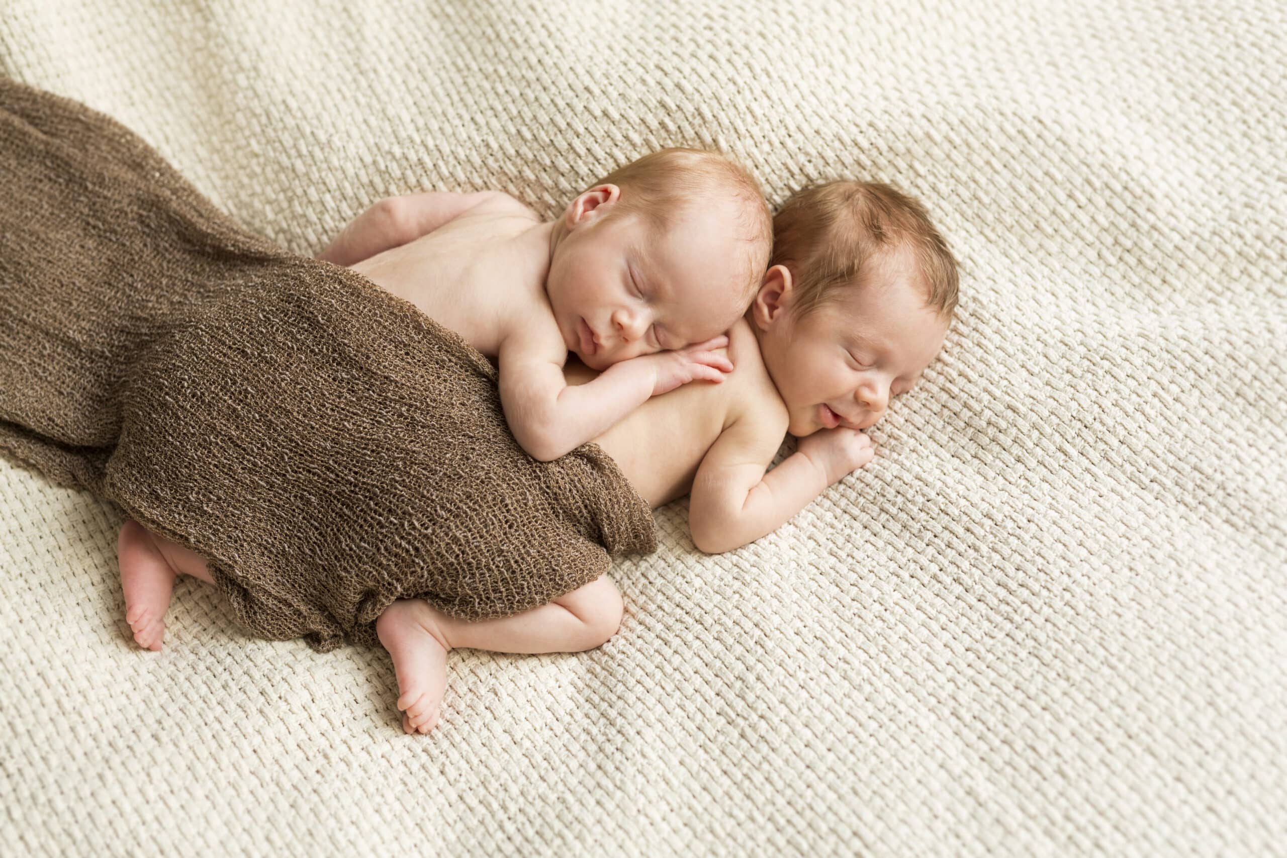 Newborn twins covered with a cloth sleeping on blanket
