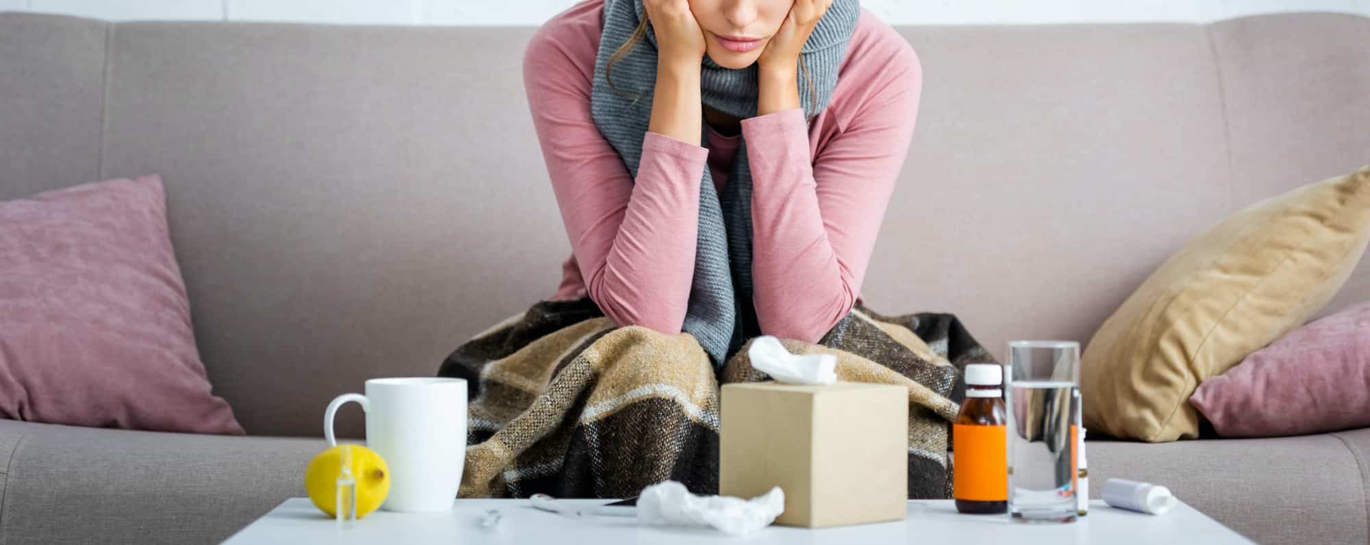 panoramic shot of ill woman with grey scarf sitting on sofa