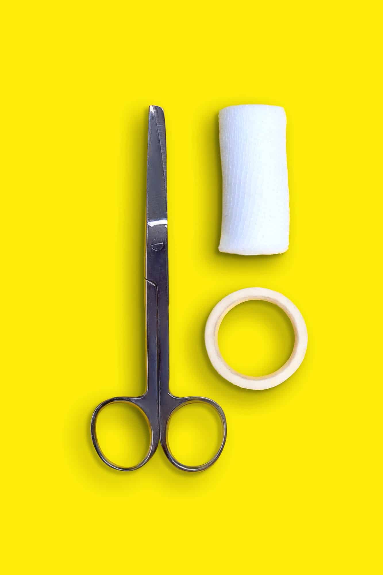 Scissors, bandages and band-aid on yellow background