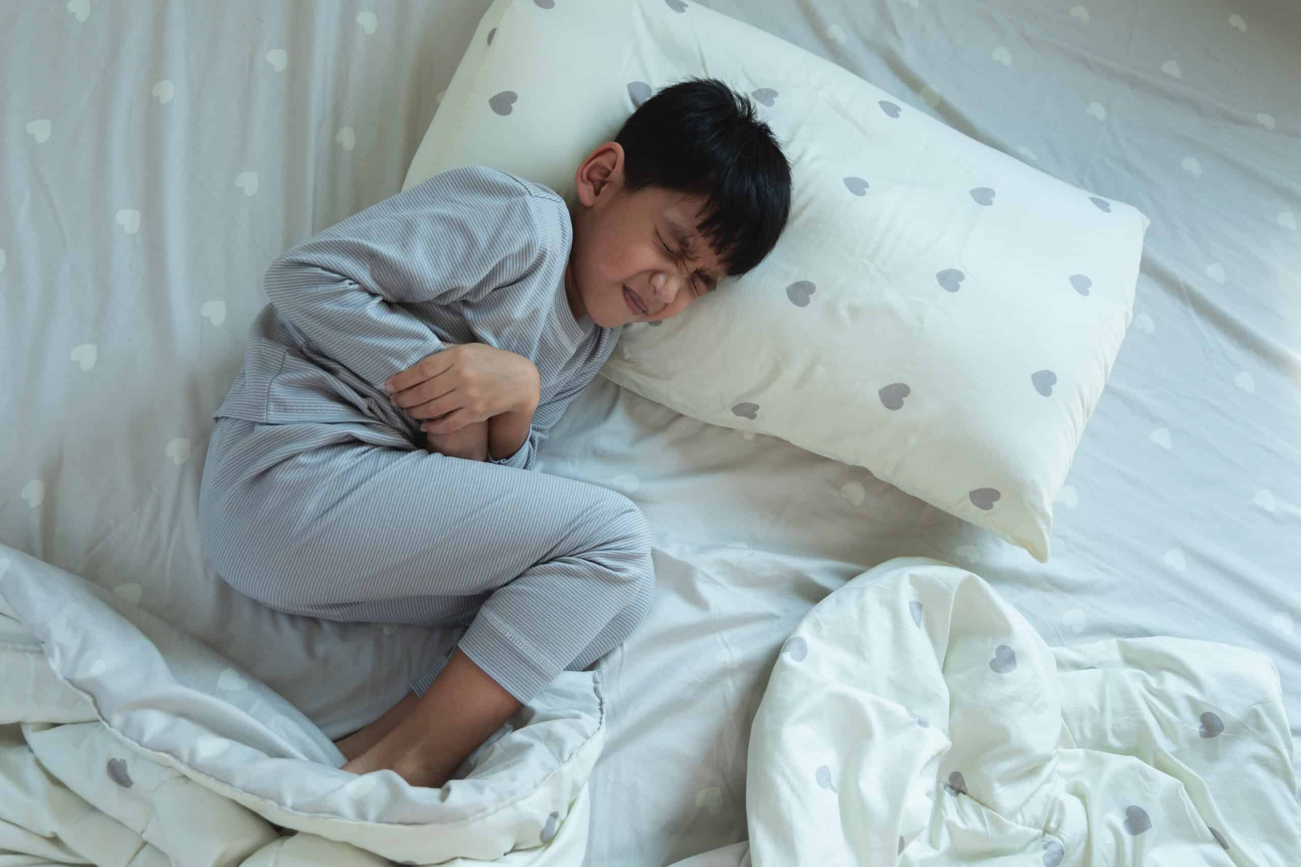 Top View of Asian boy lying in bed with stomach ache