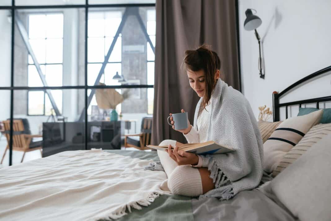Woman reading book and enjoying warm coffee in sunny apartment.