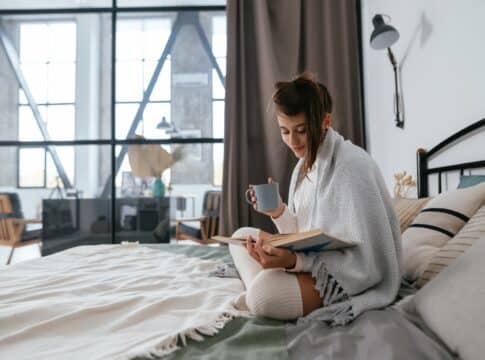 Woman reading book and enjoying warm coffee in sunny apartment.