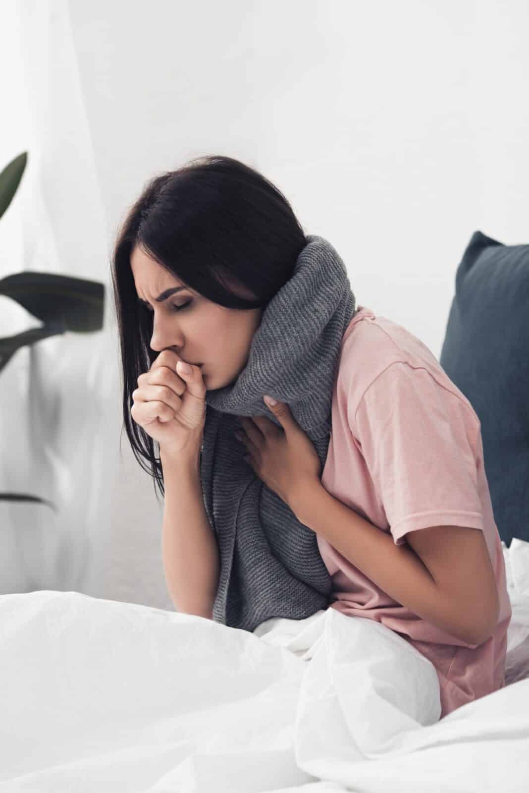 sick young woman sitting in bed and having cough