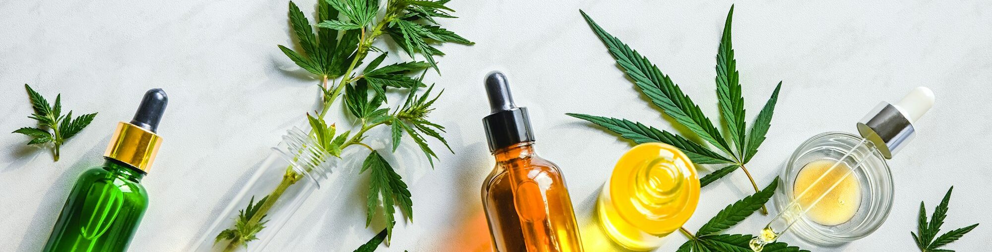 Various glass bottles with CBD oil, THC tincture hemp leaves on marble background Cosmetics CBD oil